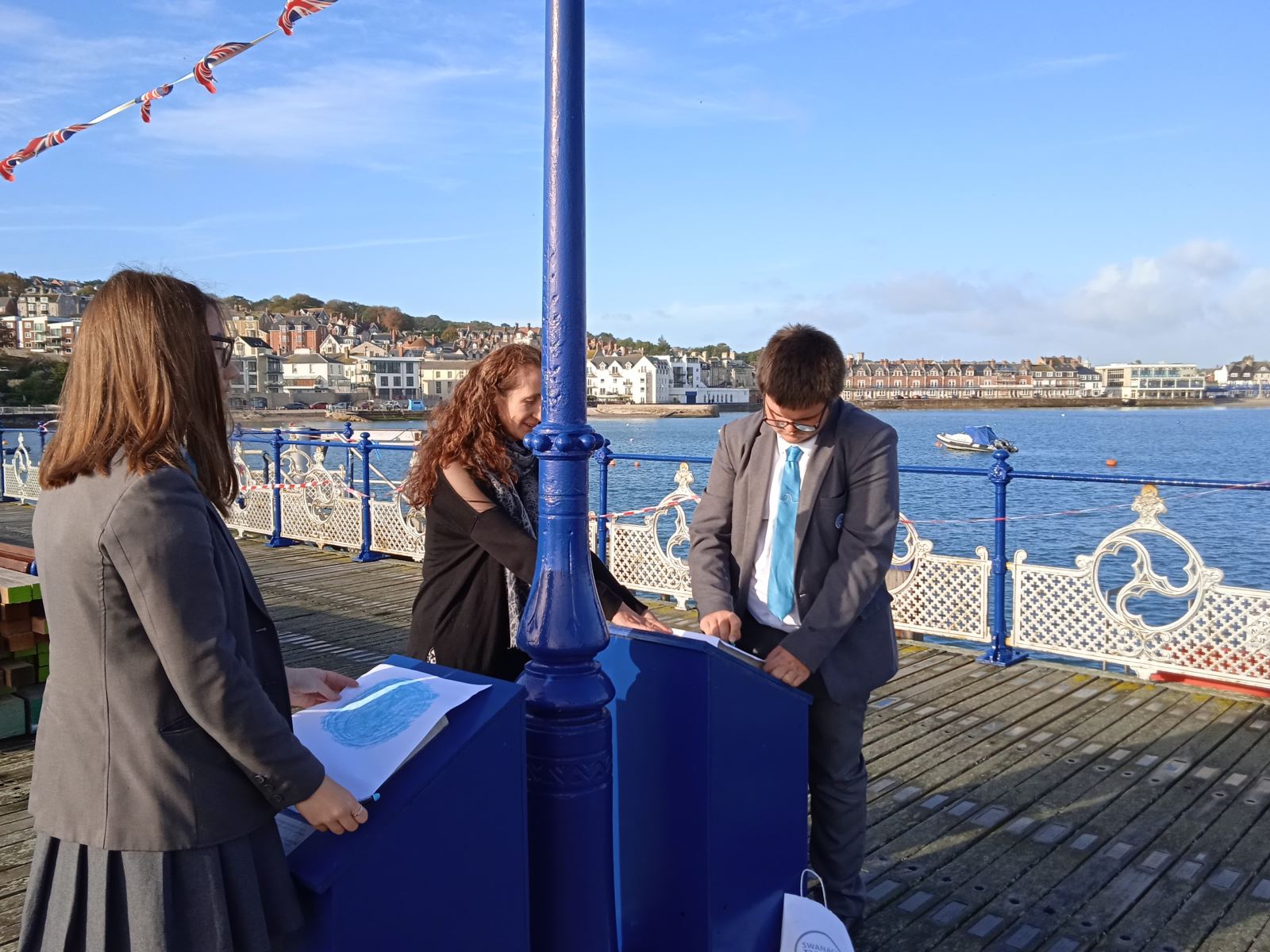 Two students and one adult do stone carving rubbings on Swanage Pier